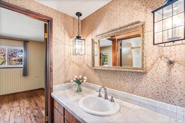 bathroom featuring a textured ceiling, wallpapered walls, vanity, and wood finished floors