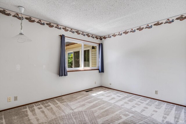 carpeted spare room featuring a textured ceiling, baseboards, and visible vents