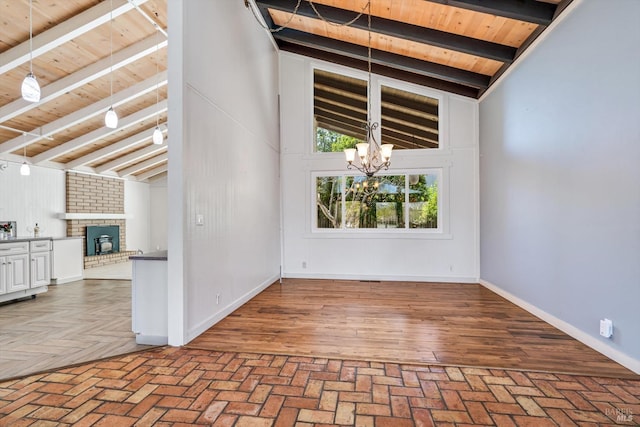 empty room featuring a brick fireplace, beam ceiling, brick floor, an inviting chandelier, and wooden ceiling