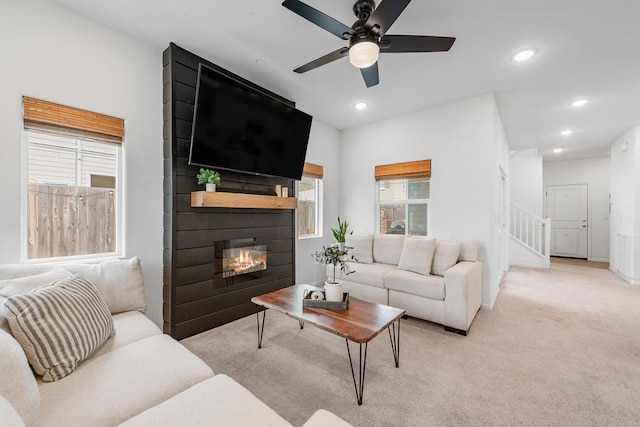 living room featuring ceiling fan, light carpet, a large fireplace, stairs, and recessed lighting