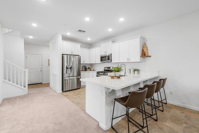 kitchen featuring visible vents, a peninsula, a kitchen breakfast bar, a sink, and appliances with stainless steel finishes