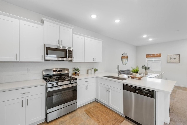 kitchen with a peninsula, recessed lighting, light countertops, a sink, and appliances with stainless steel finishes