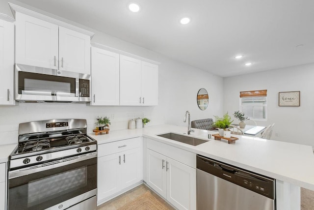 kitchen featuring appliances with stainless steel finishes, a sink, light countertops, a peninsula, and recessed lighting
