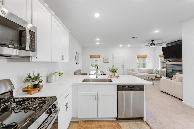 kitchen with a ceiling fan, a peninsula, a glass covered fireplace, stainless steel appliances, and recessed lighting