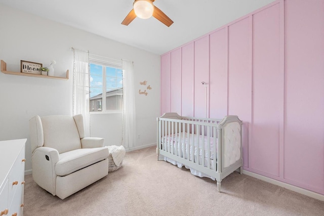 bedroom featuring a nursery area, a ceiling fan, and light colored carpet