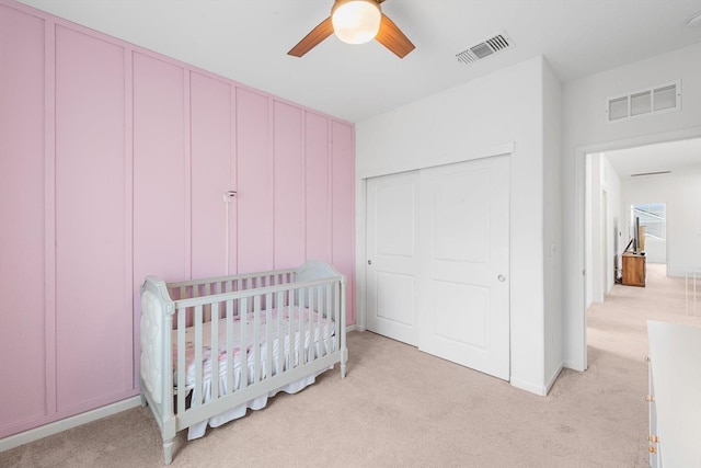 bedroom with a closet, a nursery area, light colored carpet, and visible vents