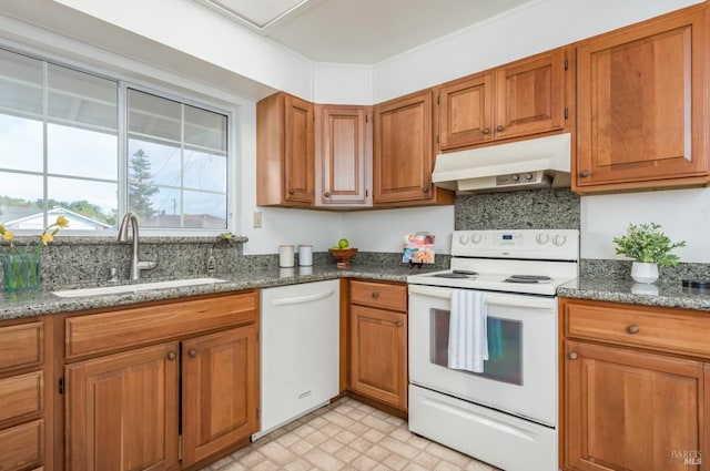 kitchen featuring a sink, brown cabinets, under cabinet range hood, dark stone countertops, and white appliances