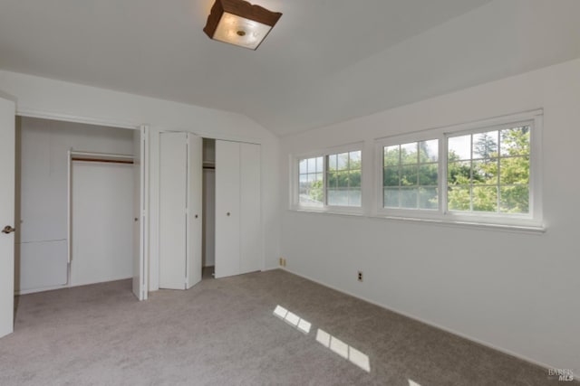 unfurnished bedroom featuring light colored carpet, multiple closets, and vaulted ceiling