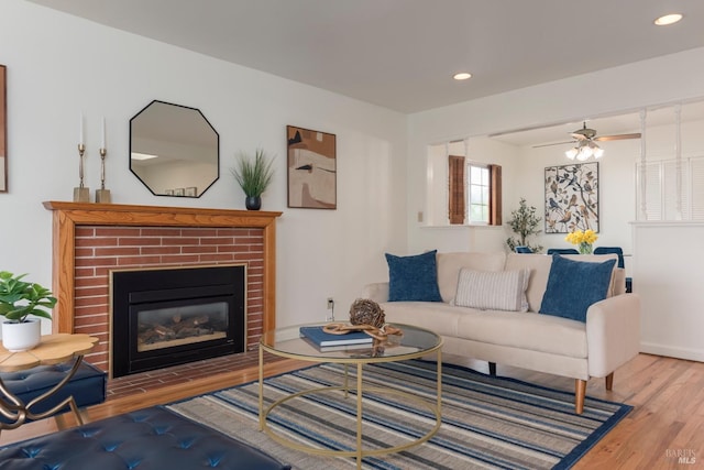 living area with a ceiling fan, wood finished floors, a brick fireplace, baseboards, and recessed lighting