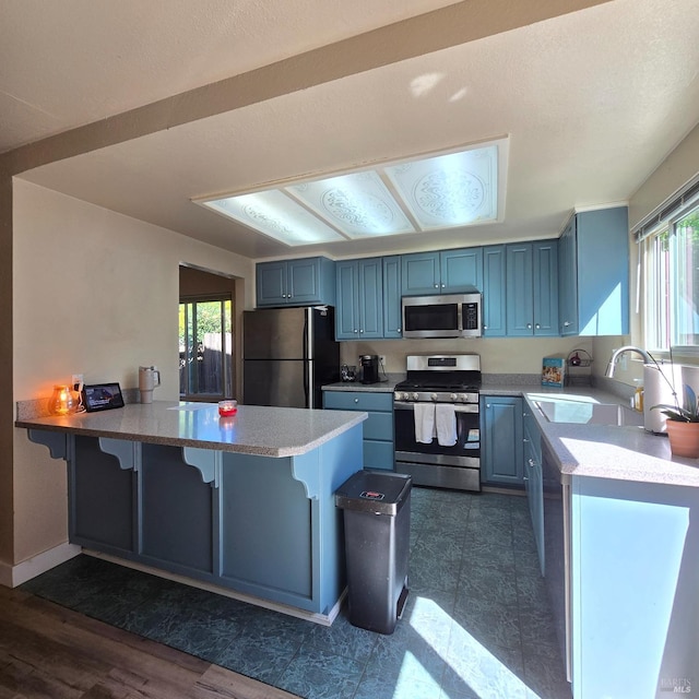 kitchen with a peninsula, plenty of natural light, appliances with stainless steel finishes, a sink, and blue cabinets