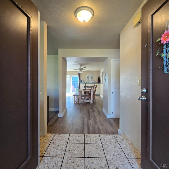 hall with tile patterned floors, baseboards, and a textured ceiling