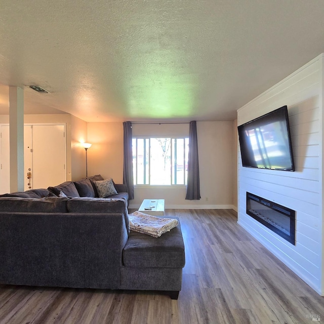living room with a textured ceiling, a fireplace, visible vents, and wood finished floors