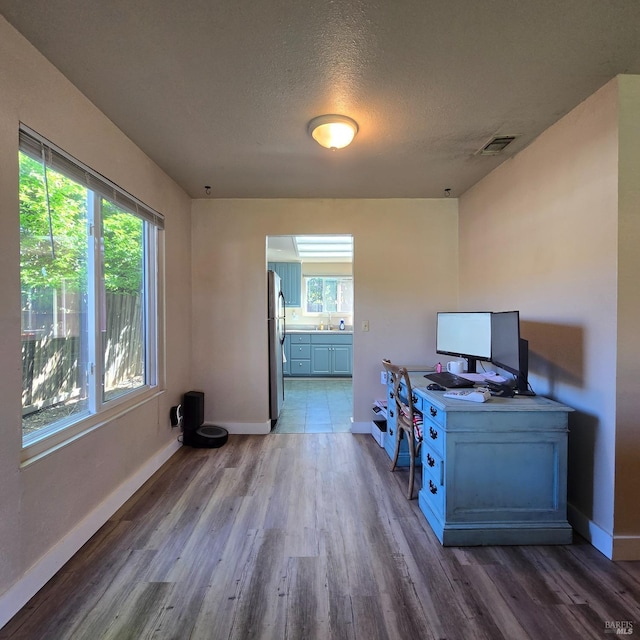 unfurnished office with baseboards, visible vents, wood finished floors, and a textured ceiling