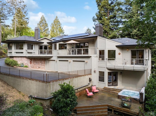 rear view of house with a chimney, a wooden deck, an attached garage, a balcony, and solar panels