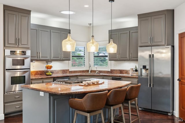 kitchen featuring light stone counters, a sink, a kitchen island, appliances with stainless steel finishes, and gray cabinetry