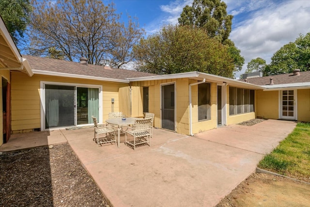 back of house with a shingled roof, a chimney, a patio area, and concrete block siding
