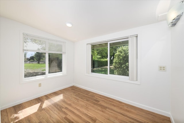 spare room featuring light wood-type flooring, baseboards, and vaulted ceiling