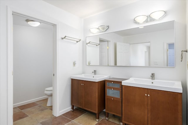 full bathroom with toilet, two vanities, a sink, and baseboards