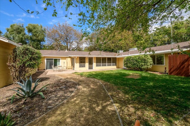 rear view of house with a sunroom, a patio area, fence, and a lawn