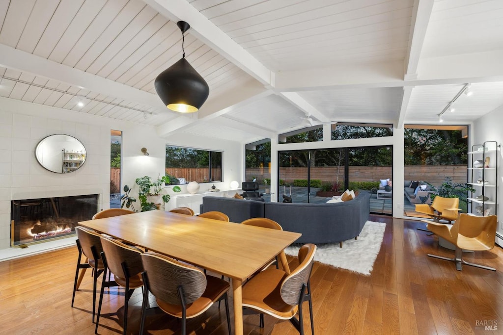 dining room featuring a fireplace, wood finished floors, rail lighting, and lofted ceiling with beams