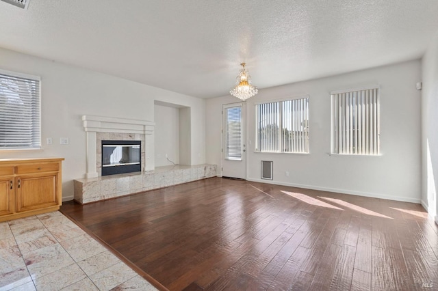 unfurnished living room with a textured ceiling, baseboards, a chandelier, and wood finished floors