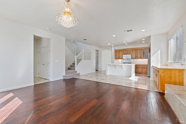 unfurnished living room featuring an inviting chandelier, light wood-style flooring, stairway, and visible vents