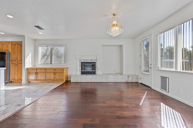 unfurnished living room featuring a premium fireplace, hardwood / wood-style floors, an inviting chandelier, a textured ceiling, and visible vents