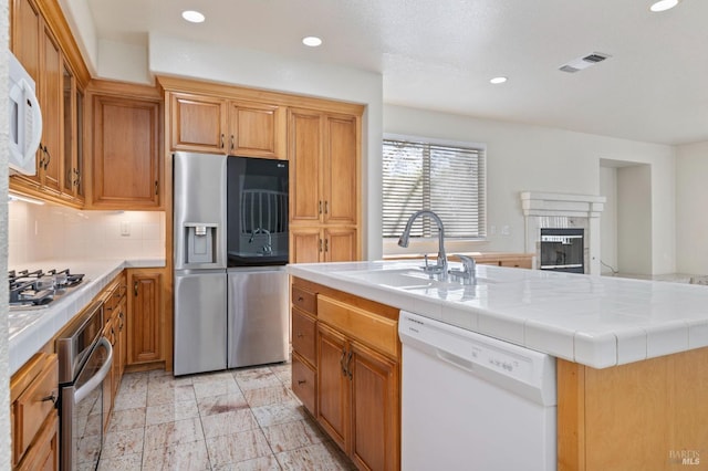 kitchen with a sink, a tile fireplace, appliances with stainless steel finishes, and recessed lighting
