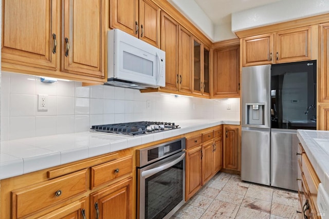 kitchen featuring tile counters, brown cabinetry, backsplash, and stainless steel appliances