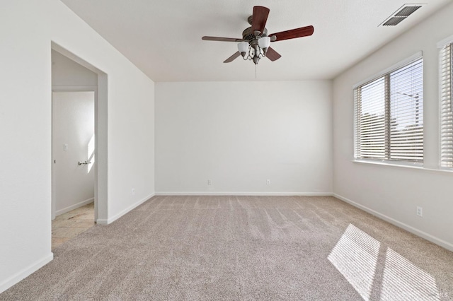 empty room featuring light colored carpet, visible vents, baseboards, and a ceiling fan