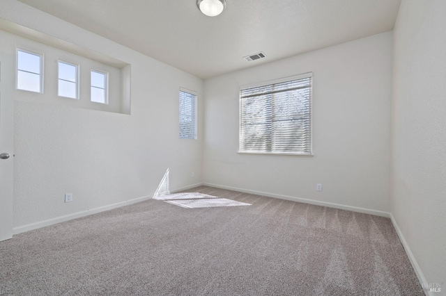 carpeted empty room featuring baseboards, visible vents, and a healthy amount of sunlight