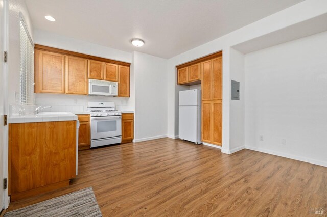 kitchen featuring electric panel, white appliances, baseboards, wood finished floors, and brown cabinets