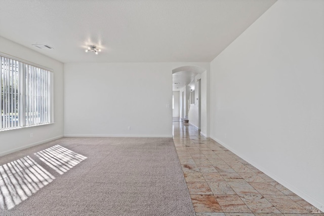 spare room with light carpet, baseboards, visible vents, and arched walkways
