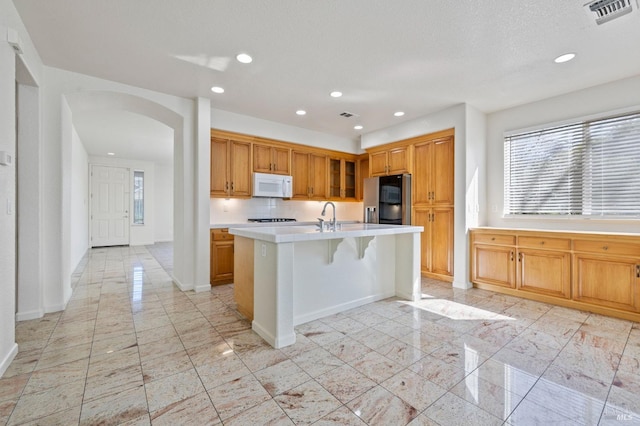 kitchen featuring light countertops, visible vents, arched walkways, stainless steel refrigerator with ice dispenser, and white microwave