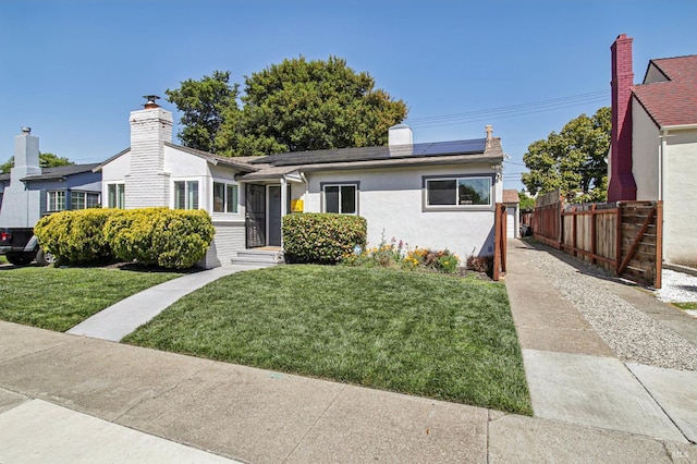 view of front of house with stucco siding, a chimney, a front yard, fence, and roof mounted solar panels