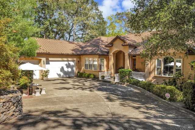 mediterranean / spanish house with covered porch, concrete driveway, stucco siding, an attached garage, and a tiled roof