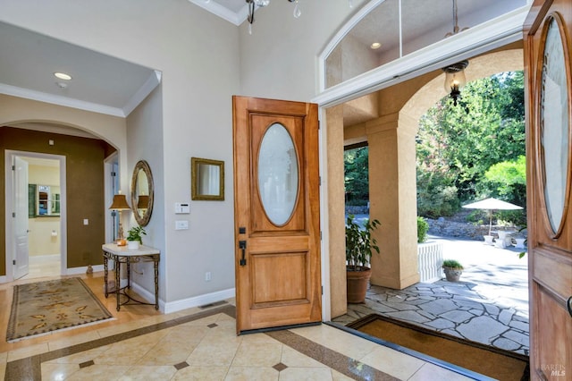 foyer featuring baseboards, arched walkways, visible vents, and crown molding