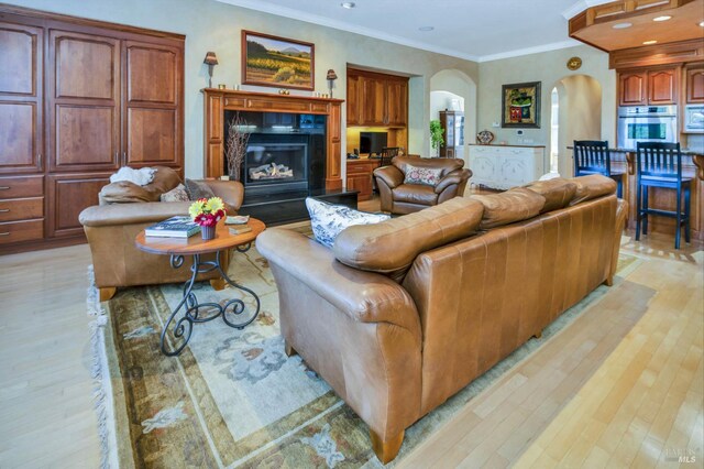 living room with a fireplace, arched walkways, crown molding, and light wood finished floors