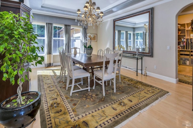 dining area with ornamental molding, wood finished floors, arched walkways, a tray ceiling, and an inviting chandelier