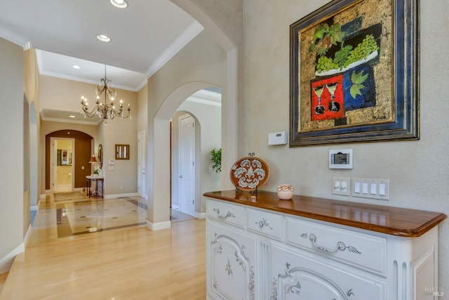 hallway featuring ornamental molding, baseboards, a chandelier, arched walkways, and light wood-style flooring