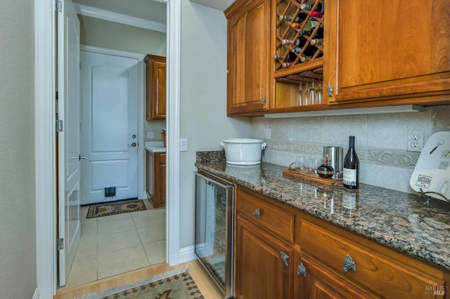 kitchen featuring light tile patterned flooring, beverage cooler, brown cabinetry, decorative backsplash, and dark stone counters