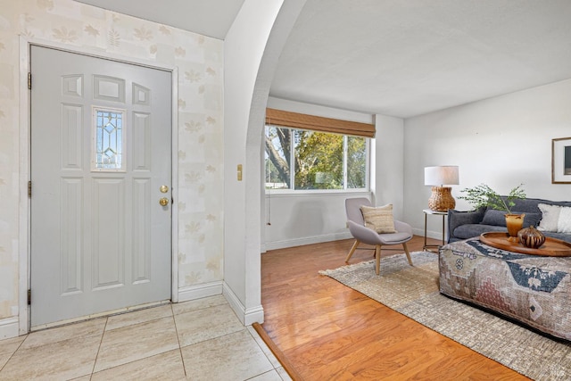 entryway featuring arched walkways, baseboards, wallpapered walls, and wood finished floors