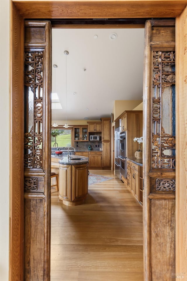 kitchen with an island with sink, light wood-style flooring, a sink, stainless steel appliances, and brown cabinets