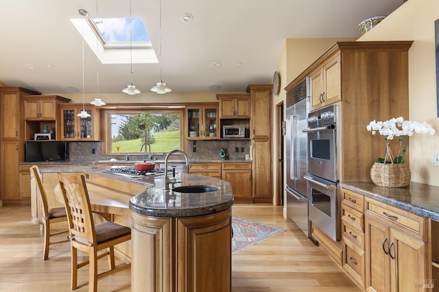 kitchen with glass insert cabinets, a sink, brown cabinetry, and appliances with stainless steel finishes