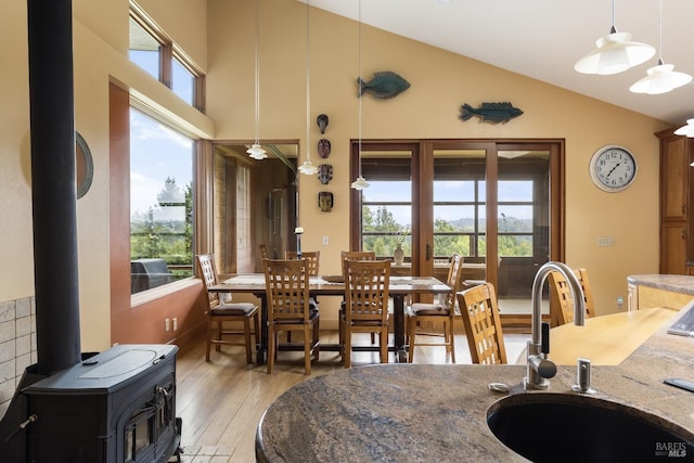 dining room featuring light wood-style floors, high vaulted ceiling, and a wood stove