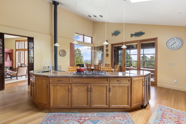 kitchen with an island with sink, light wood-style flooring, stainless steel gas stovetop, a sink, and brown cabinets