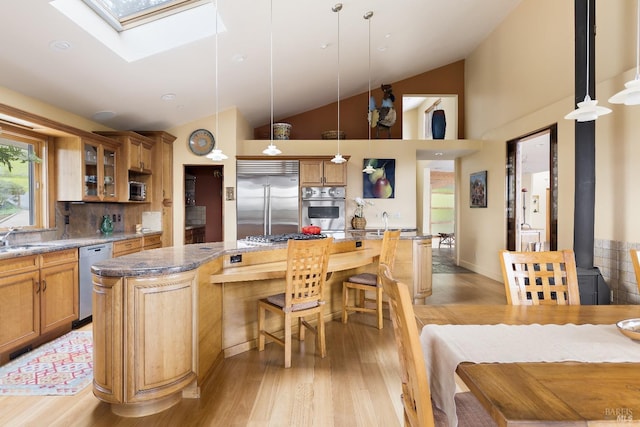 kitchen featuring glass insert cabinets, an island with sink, a kitchen bar, light wood finished floors, and stainless steel appliances