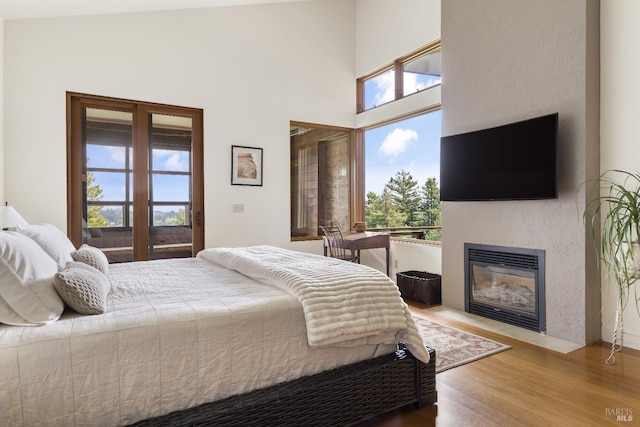 bedroom with a glass covered fireplace, a high ceiling, and wood finished floors
