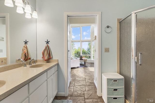 full bathroom with stone finish flooring, a sink, a stall shower, double vanity, and baseboards