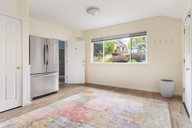unfurnished bedroom featuring baseboards, freestanding refrigerator, vaulted ceiling, and wood finished floors